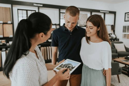 Couple meeting with a home consultant in a design center while reviewing a photorealistic home rendering on a tablet.