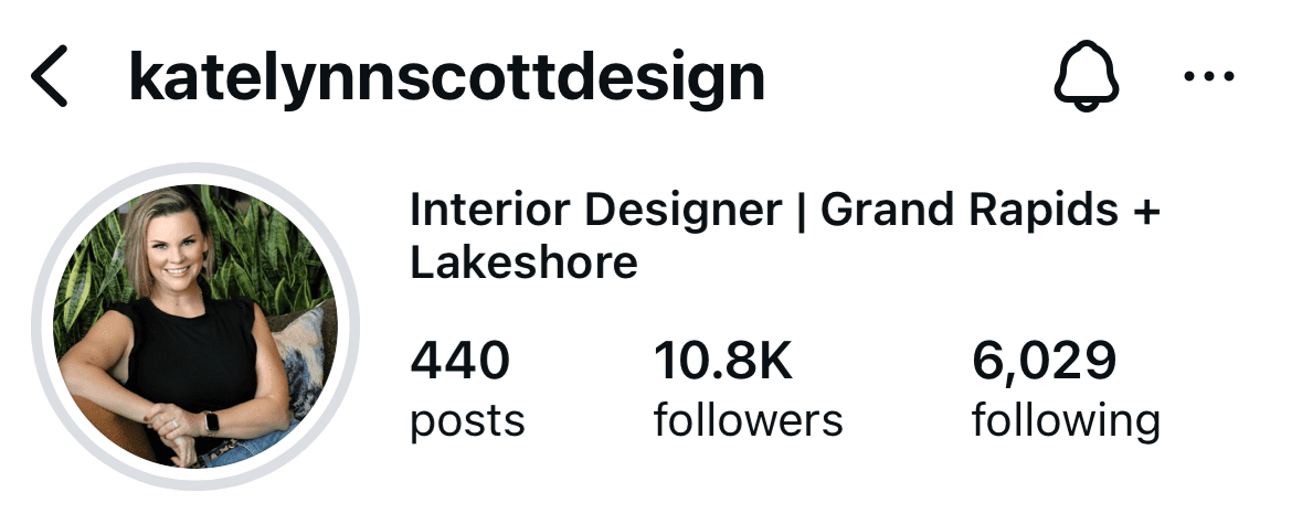 Instagram profile photo of Katelynn Scott, interior designer — smiling in a sleeveless black top with green foliage behind.